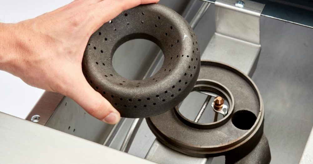 A person disassembling a metal gas range on a commercial oven. The person holds the metal burner in their hand.