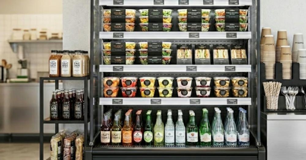 A tall black commercial open air cooler full of food and drinks. The cooler is installed inside a shop.