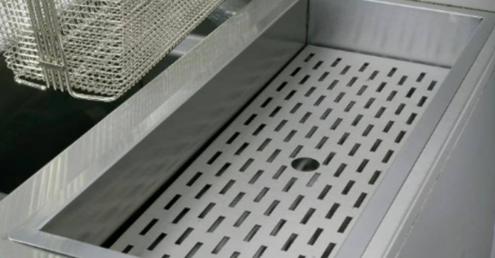 A clean commercial fryer in a restaurant kitchen. An empty, clean fryer basket sits in a nearby holder.