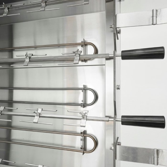 Two metal spits inside a commercial rotisserie oven. The rotisserie oven is inside a brightly lit kitchen.