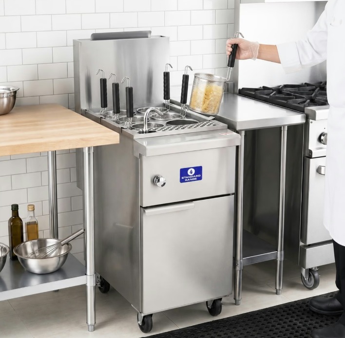 A chef removes a container from a pasta cooker. Five more containers remain immersed in the cooking machine.
