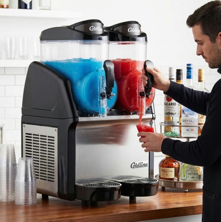 A red icee machine and a blue icee machine on a countertop. A customer pours a red icee from the machine.