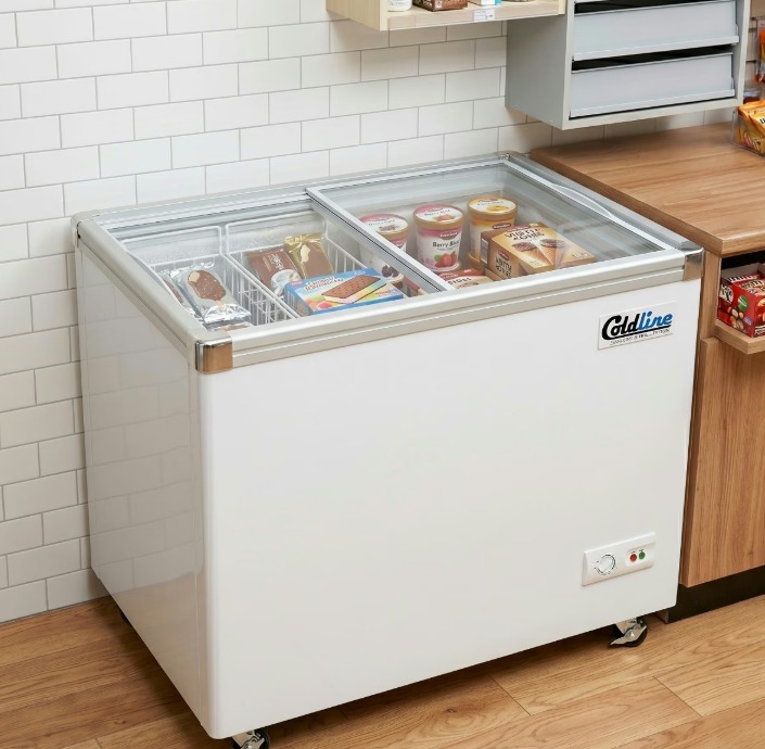 A short, white freezer installed next to a wooden counter in a brightly lit shop. The freezer is full of ice cream.