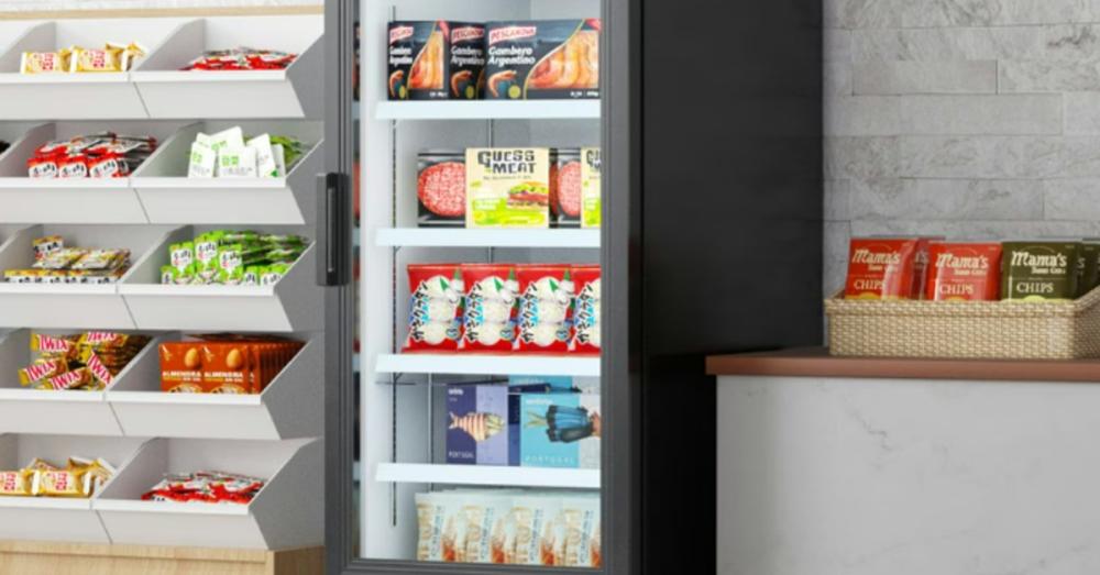 A single-door merchandizer freezer with a glass door in a shop. The freezer is full of ice cream and frozen food.