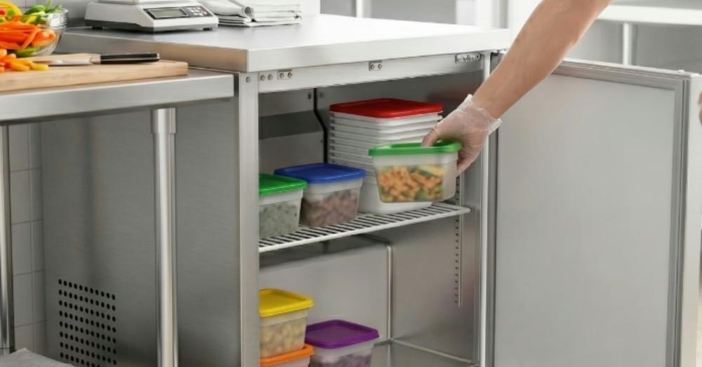 A small undercounter freezer in a commercial kitchen. An employee removes a package of food from the freezer.