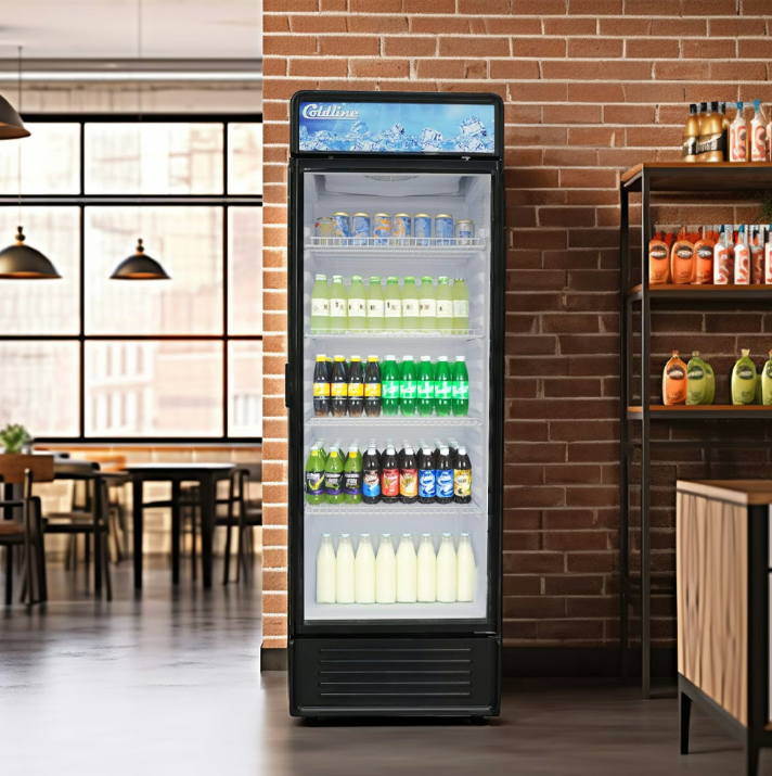A tall reach-in refrigerator in the middle of a brightly lit shop. The refrigerator is full of colorful drinks.