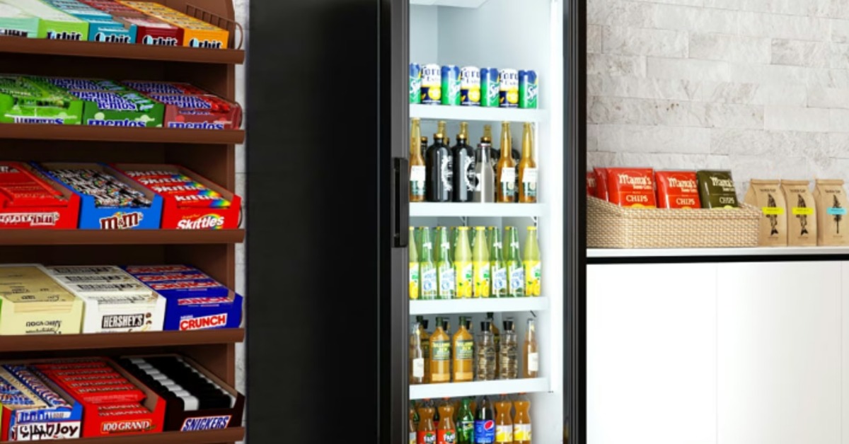 A reach-in refrigerator between candy bars and chips in a convenience store. The fridge is full of drinks.